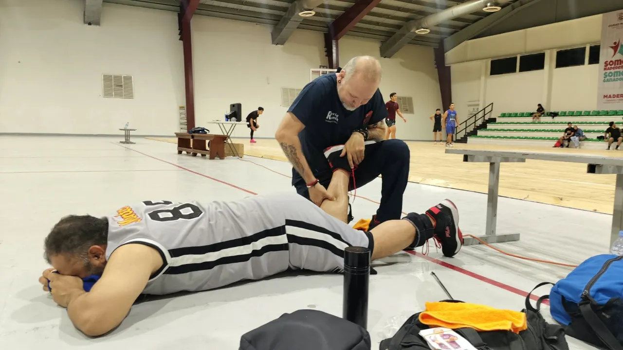 David Runik sostiene la pierna de un jugador recostado y le da atención en una cancha de básquetbol